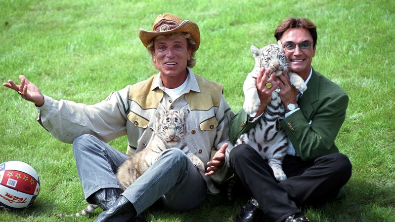 1997: Siegfried und Roy mit zwei Tigerjungen. Die beiden Magier sind für die Zucht weißer Tiger bekannt. | Bild: dpa-Bildfunk/Boris Roessler 1997: Siegfried und Roy mit zwei Tigerjungen. Die beiden Magier sind für die Zucht weißer Tiger bekannt.