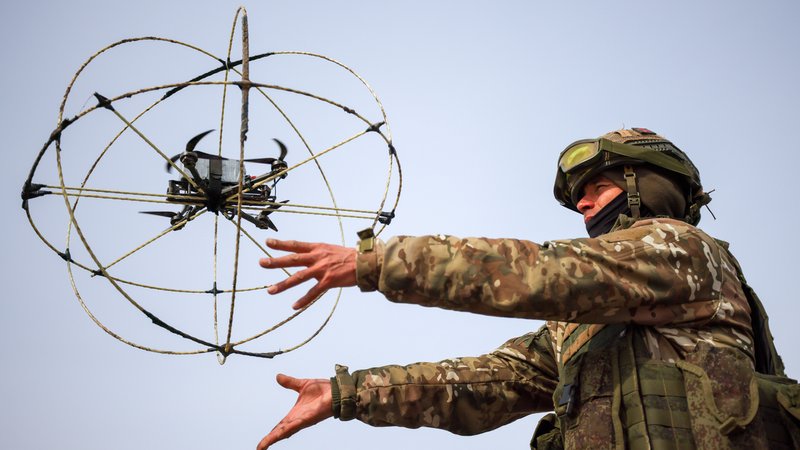 Uniformierter in Kampfmontur mit fliegender Drohne, um die ein Abstandsgitter gelegt ist | Bild: Alexander Reka/Picture Alliance Uniformierter in Kampfmontur mit fliegender Drohne, um die ein Abstandsgitter gelegt ist