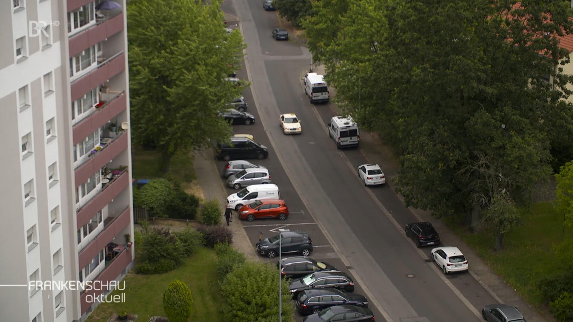 Blick von oben auf eine von Bäumen gesäumte Straße, wo Autos parken. 