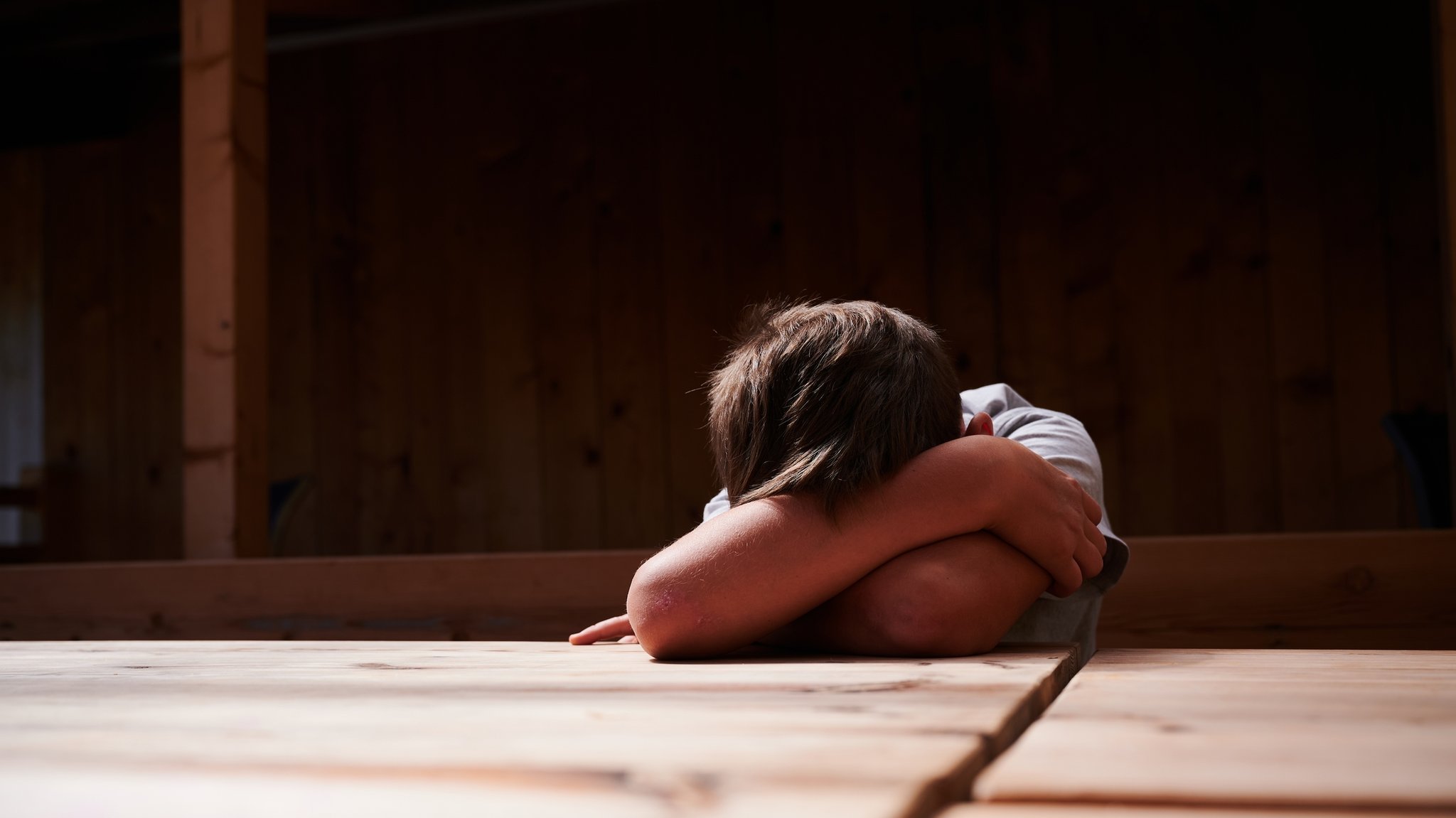 Ein Bub sitzt an einem Tisch und verdeckt sein Gesicht mit den Armen (Symbolbild)