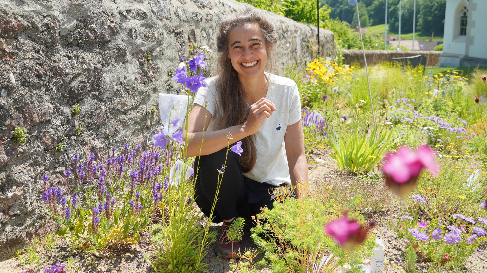 Biologin Fabienne Maihoff kniet inmitten einer Staudenfläche in Schönau an der Brend – um sie herum bunte Blumen