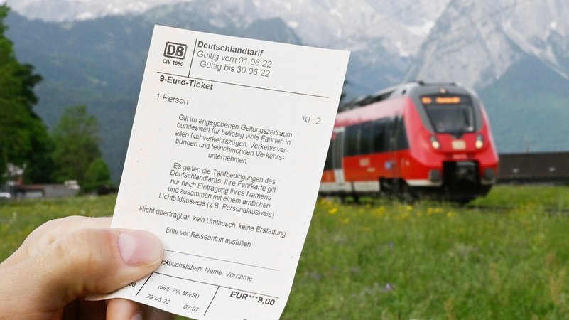 ARCHIV - 23.05.2022, Bayern, Garmisch-Partenkirchen: Ein Mann hält ein 9-Euro-Ticket in der Hand, im Hintergrund fährt ein Zug der Deutschen Bahn vor der Bergkulisse des Wettersteingebirges vorbei (gestelltes Foto). (zu dpa: «Halbzeit beim 9-Euro-Ticket: Licht und Schatten») Foto: Angelika Warmuth/dpa +++ dpa-Bildfunk +++ | Bild: dpa-Bildfunk/Angelika Warmuth ARCHIV - 23.05.2022, Bayern, Garmisch-Partenkirchen: Ein Mann hält ein 9-Euro-Ticket in der Hand, im Hintergrund fährt ein Zug der Deutschen Bahn vor der Bergkulisse des Wettersteingebirges vorbei (gestelltes Foto). (zu dpa: «Halbzeit beim 9-Euro-Ticket: Licht und Schatten») Foto: Angelika Warmuth/dpa +++ dpa-Bildfunk +++
