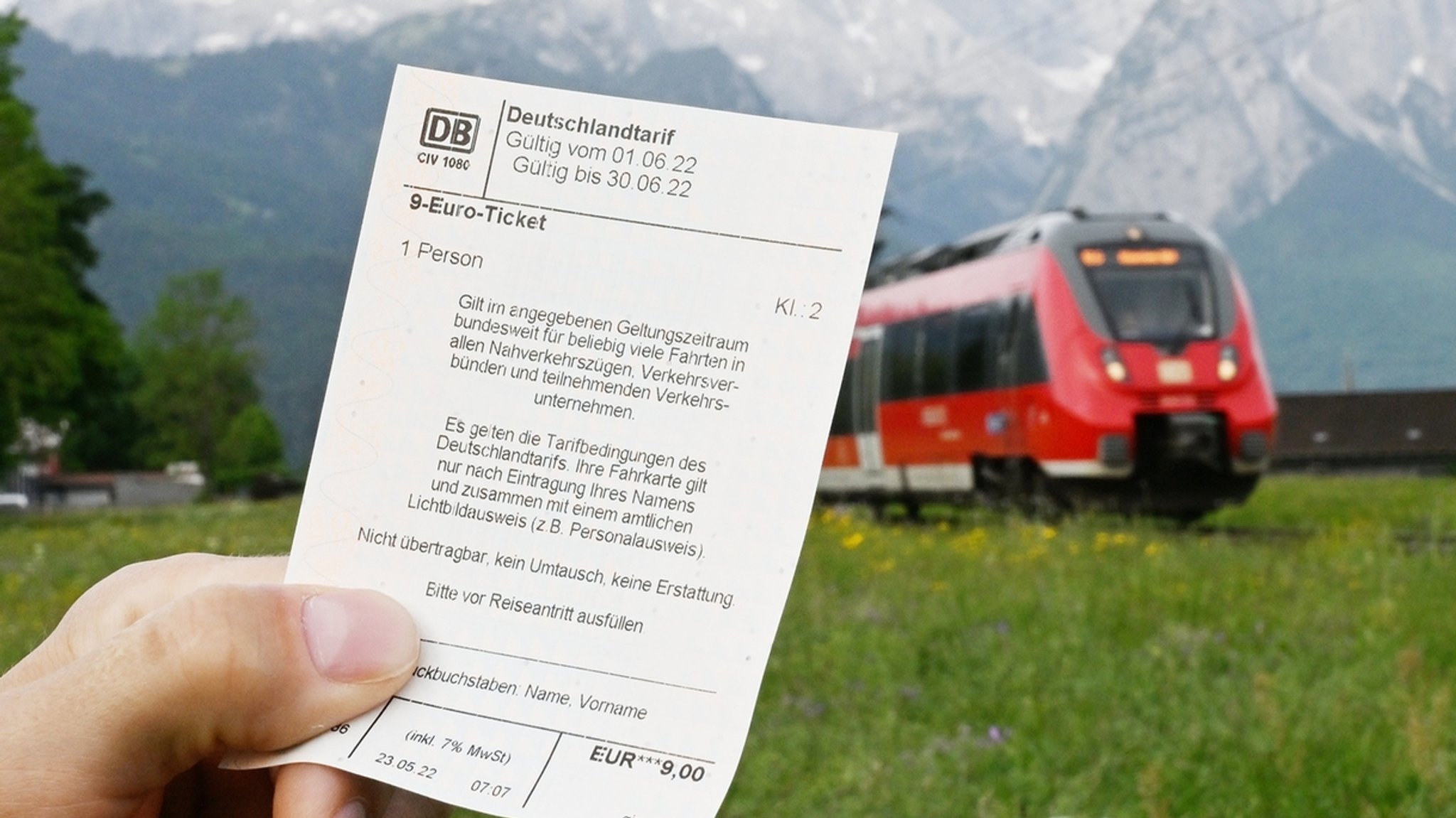 ARCHIV - 23.05.2022, Bayern, Garmisch-Partenkirchen: Ein Mann hält ein 9-Euro-Ticket in der Hand, im Hintergrund fährt ein Zug der Deutschen Bahn vor der Bergkulisse des Wettersteingebirges vorbei (gestelltes Foto). (zu dpa: «Halbzeit beim 9-Euro-Ticket: Licht und Schatten») Foto: Angelika Warmuth/dpa +++ dpa-Bildfunk +++