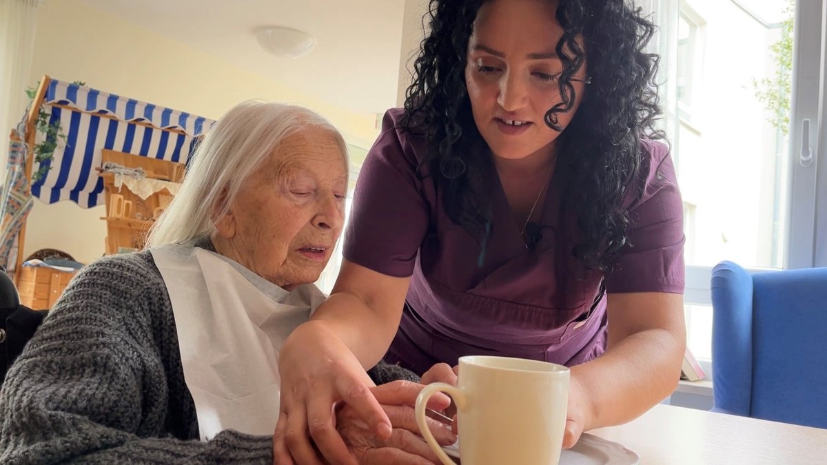 Pflegefachkraft Aferdita Bajraliu-Sulejmani hilft einer Seniorin beim Kaffeetrinken.