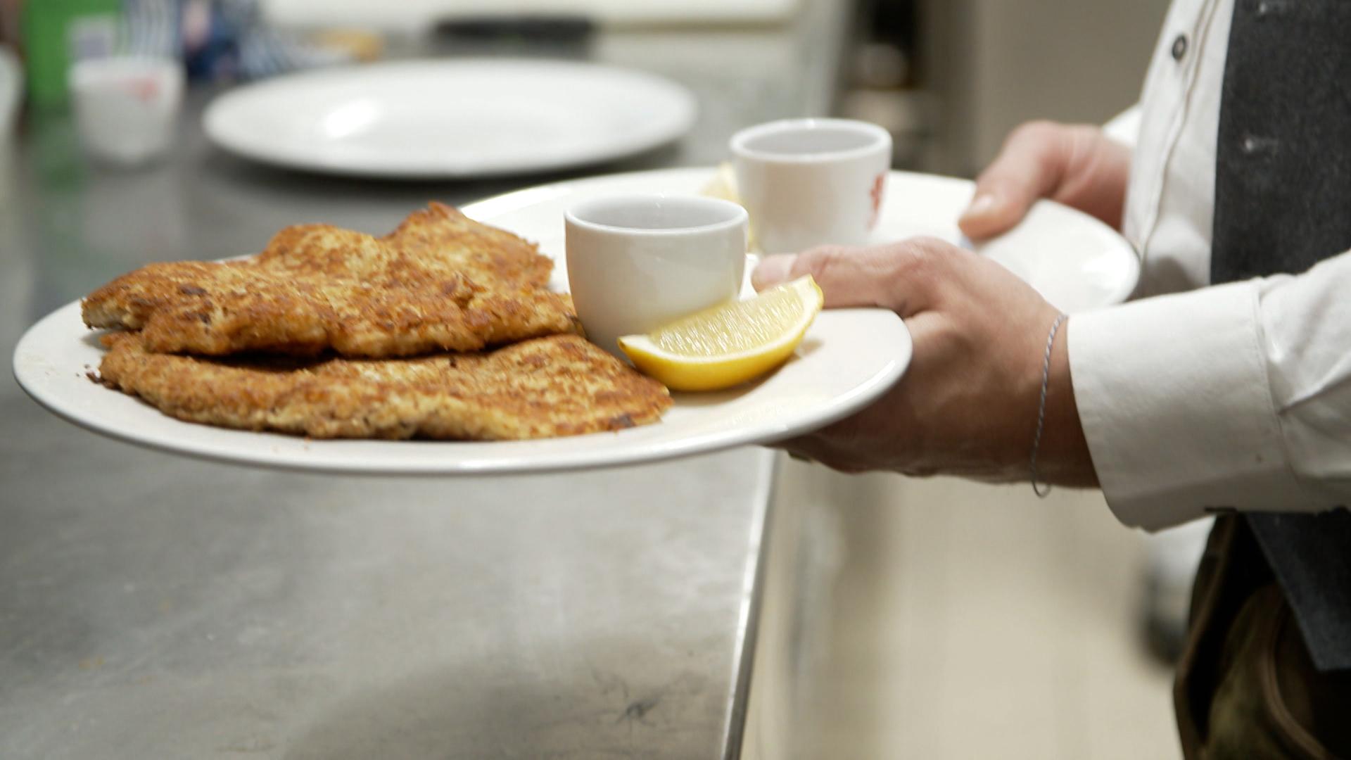 Person trägt zwei Teller mit Wiener Schnitzel