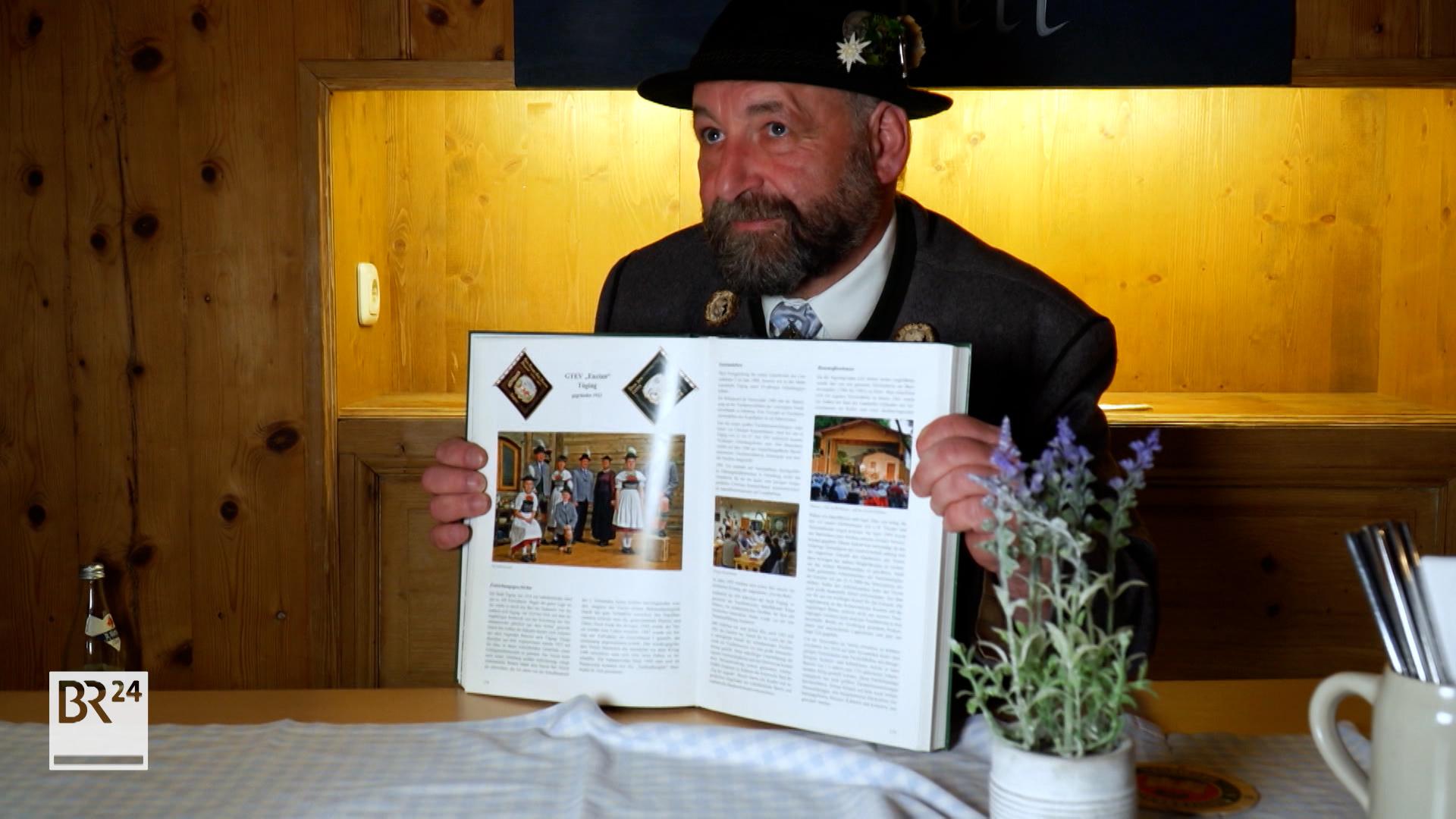 Der zuständige Gauvorstand, Michael Hauser.  Er trägt Trachtenhut, sitzt an einem Tisch und hält ein aufgeklapptes Buch in den Händen.