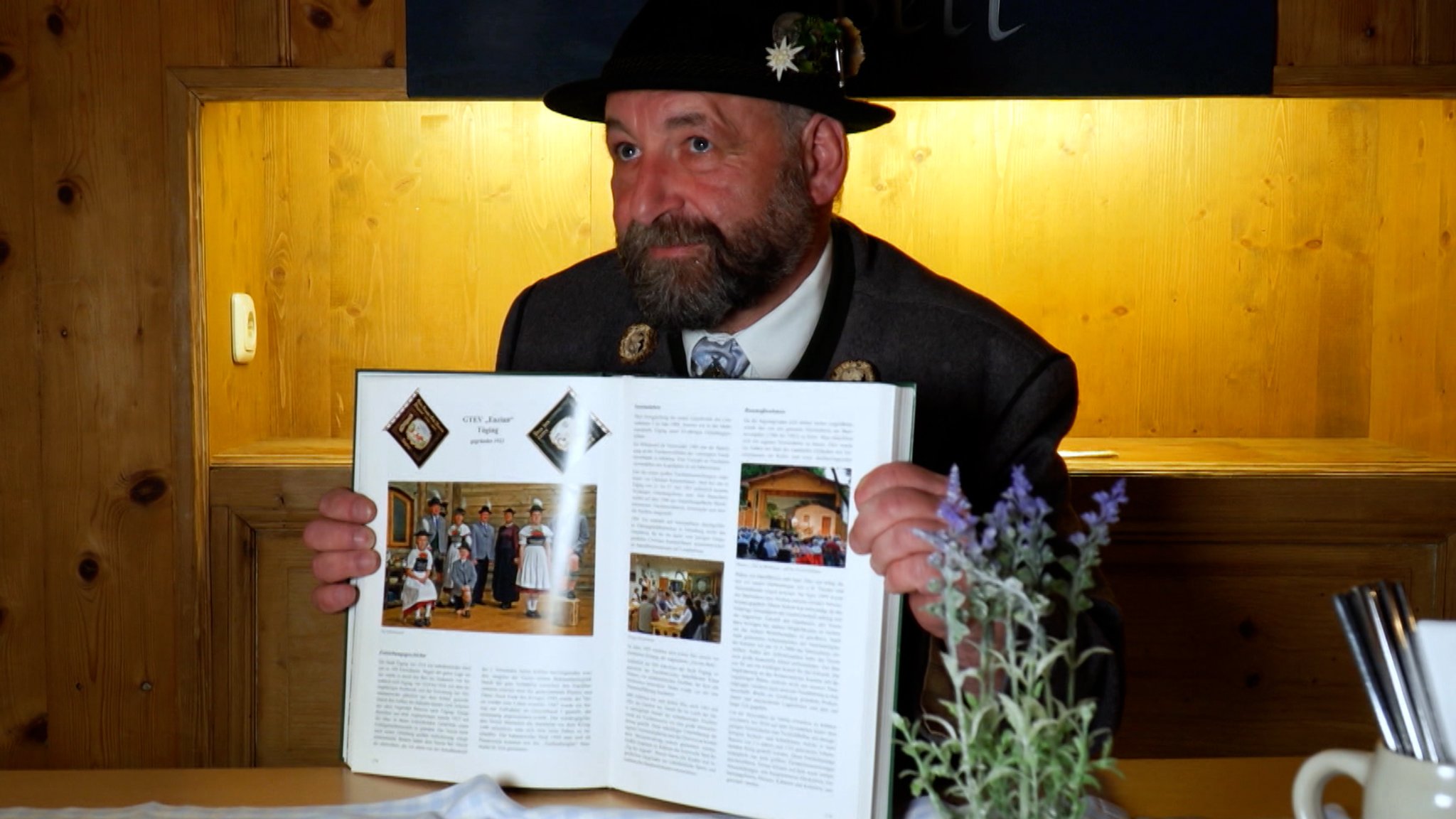 Der zuständige Gauvorstand, Michael Hauser.  Er trägt Trachtenhut, sitzt an einem Tisch und hält ein aufgeklapptes Buch in den Händen.