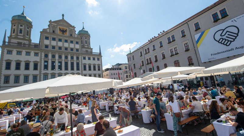 Zahlreiche Menschen treffen sich auf dem Rathausplatz zur gemeinsamen Friedenstafel anlässlich des Friedensfests der Stadt Augsburg.