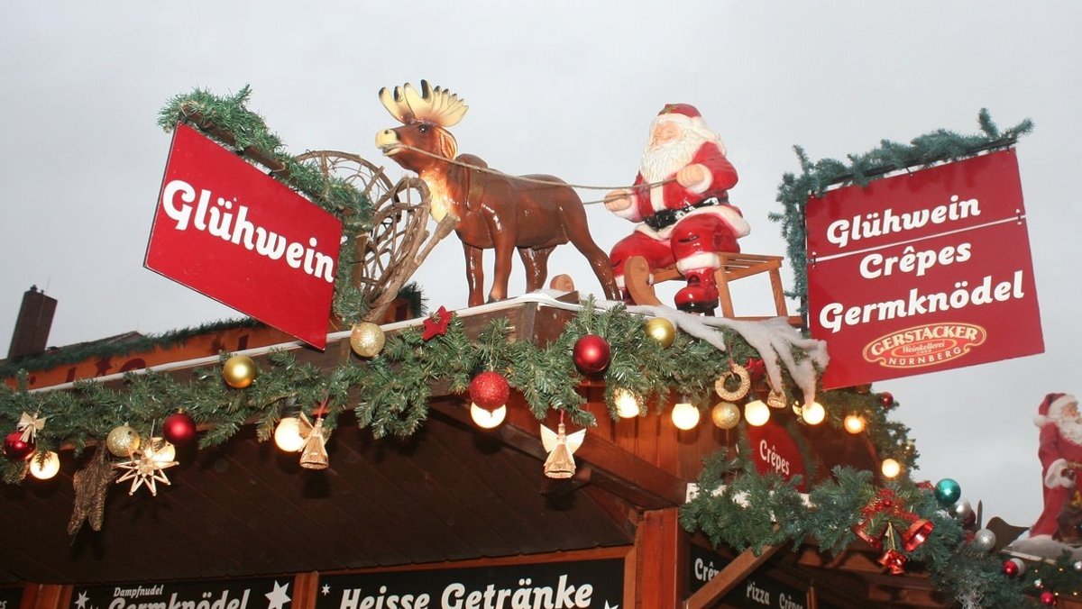 Auf dem Dach einer Weihnachtsbude aus Holz sind Schilder mit der Aufschrift "Glühwein" zu sehen und ein Nikolaus auf einem Schlitten.