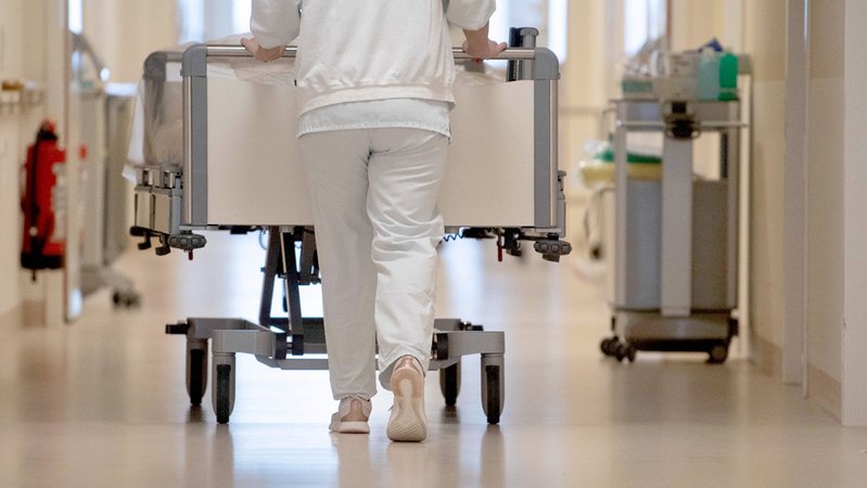 Eine Krankenpflegerin schiebt in einem Krankenhaus ein Krankenbett durch einen Flur. 