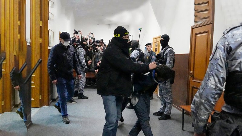 Ein Mann mit verbundenen Augen und in gebückter Haltung wird durch einen Raum geführt | Bild: Bayerischer Rundfunk 2024 Ein Mann mit verbundenen Augen und in gebückter Haltung wird durch einen Raum geführt