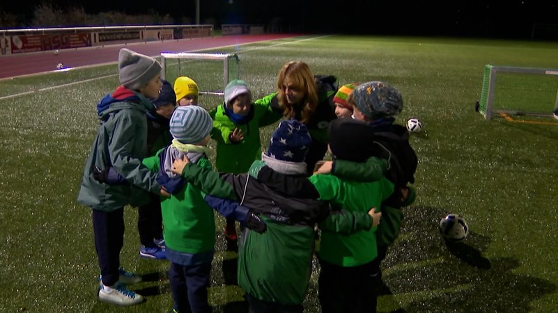 Die ehrenamtliche Trainerin steht gemeinsam mit ihrem Kinder-Fußballteam im Kreis beim Training. | Bild: BR Die ehrenamtliche Trainerin steht gemeinsam mit ihrem Kinder-Fußballteam im Kreis beim Training.