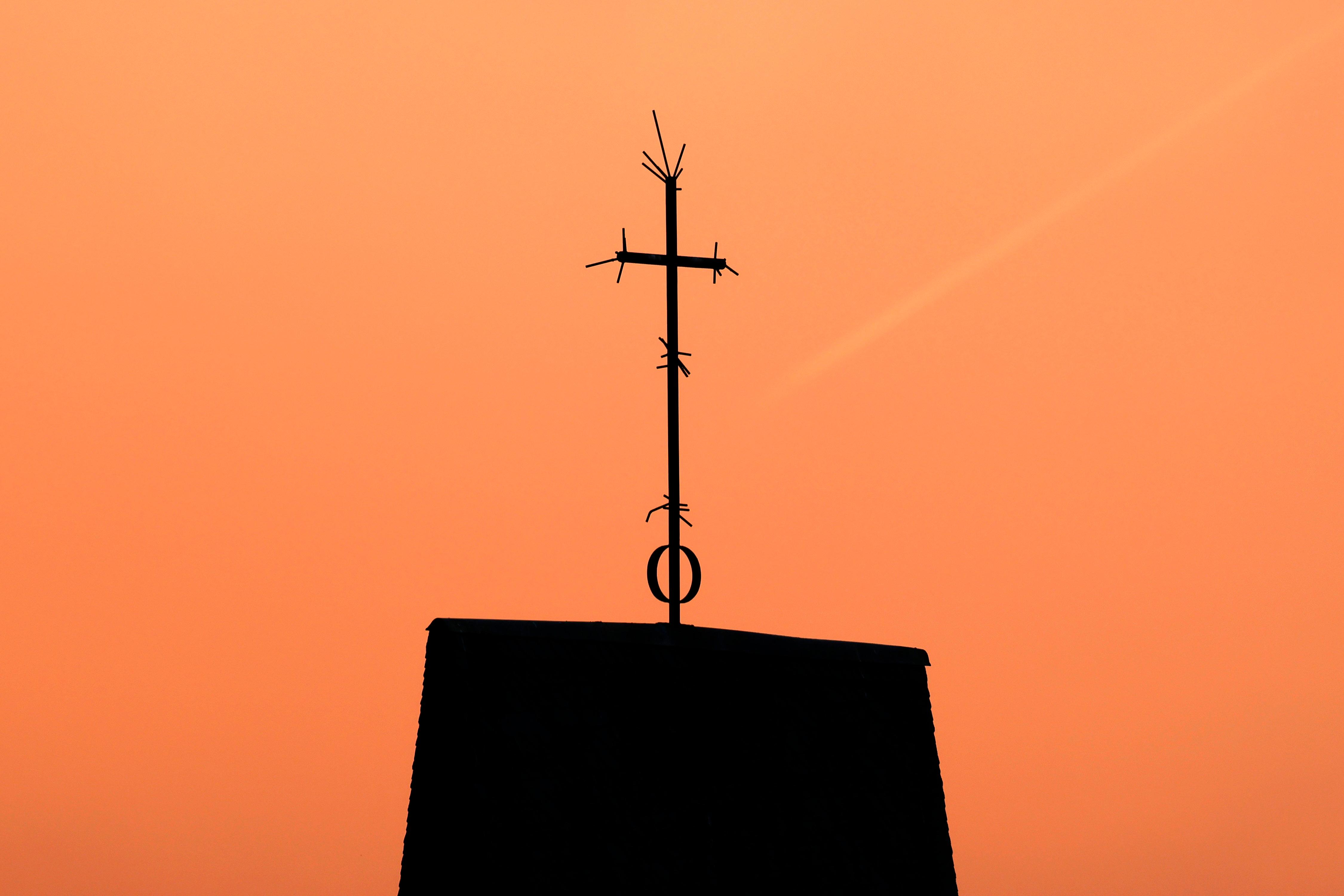 Symbolbild: Ein Kreuz steht auf dem Dach einer Kirche vor Abendhimmel.