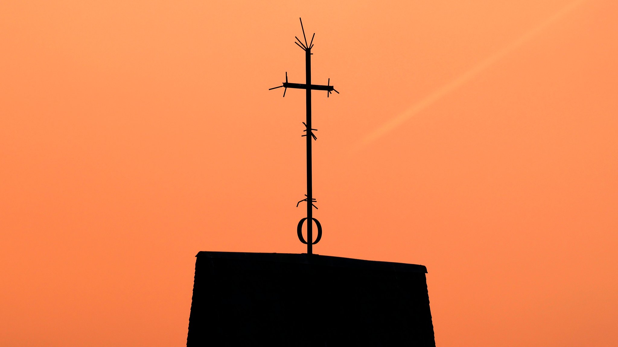 Symbolbild: Ein Kreuz steht auf dem Dach einer Kirche vor Abendhimmel.