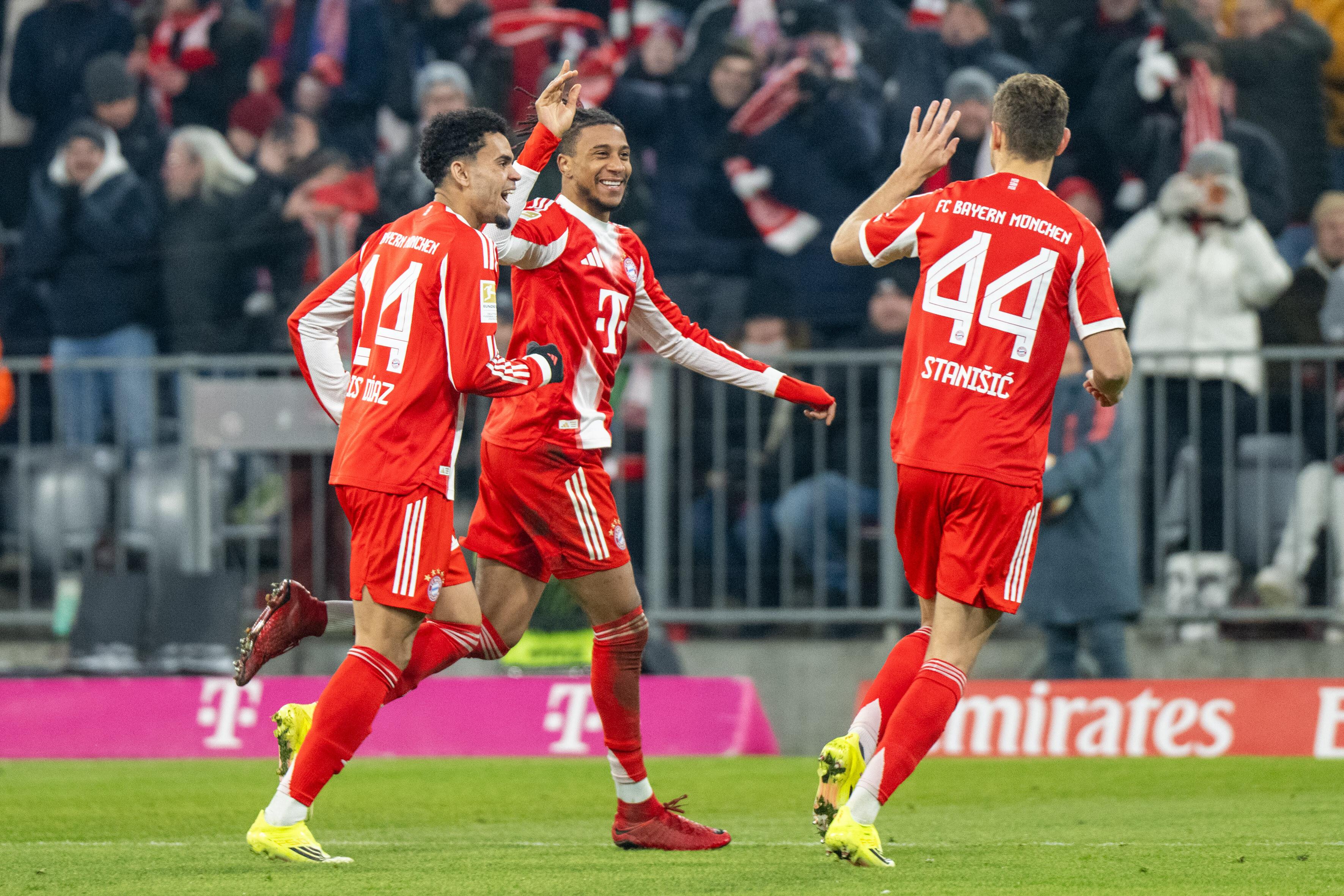 Michael Olise (Mitte) feiert ein Tor für den FC Bayern München gegen den VfL Wolfsburg mit Luis Diaz (links) und Josip Stanisic (rechts).