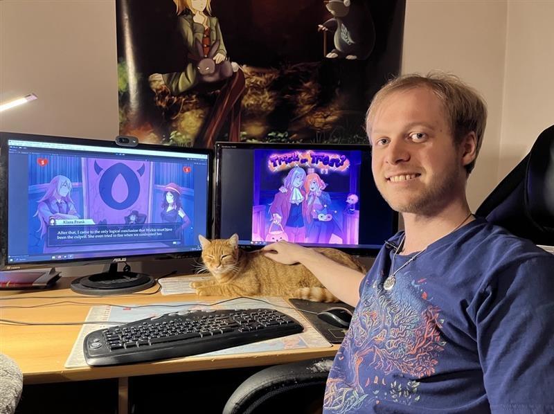Maximilian Abstreiter mit seiner Katze vor zwei Bildschirmen.