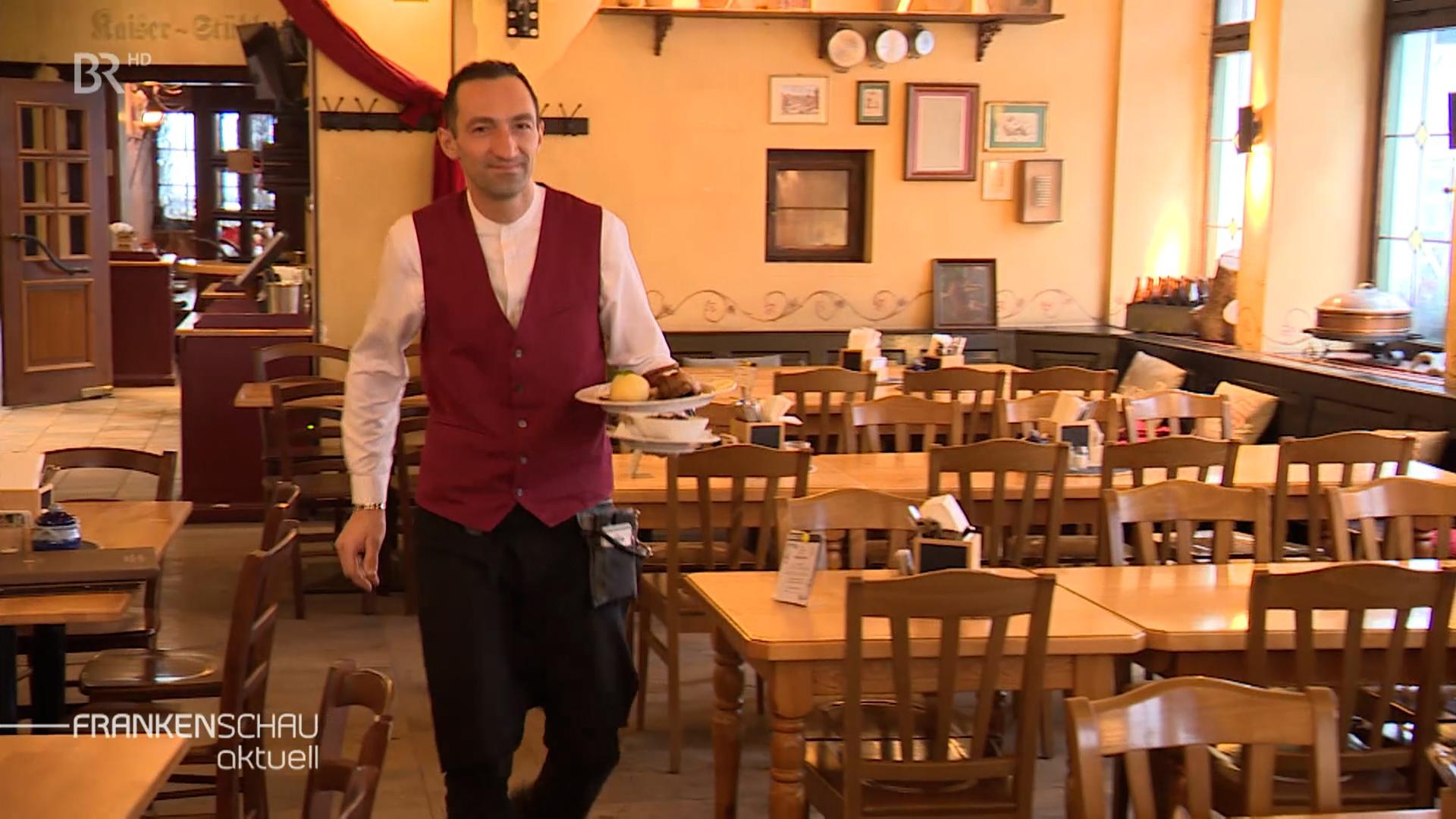 Ein Kellner trägt einen Teller mit Essen durch einen leeren Gastraum