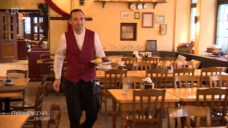 Ein Kellner trägt einen Teller mit Essen durch einen leeren Gastraum