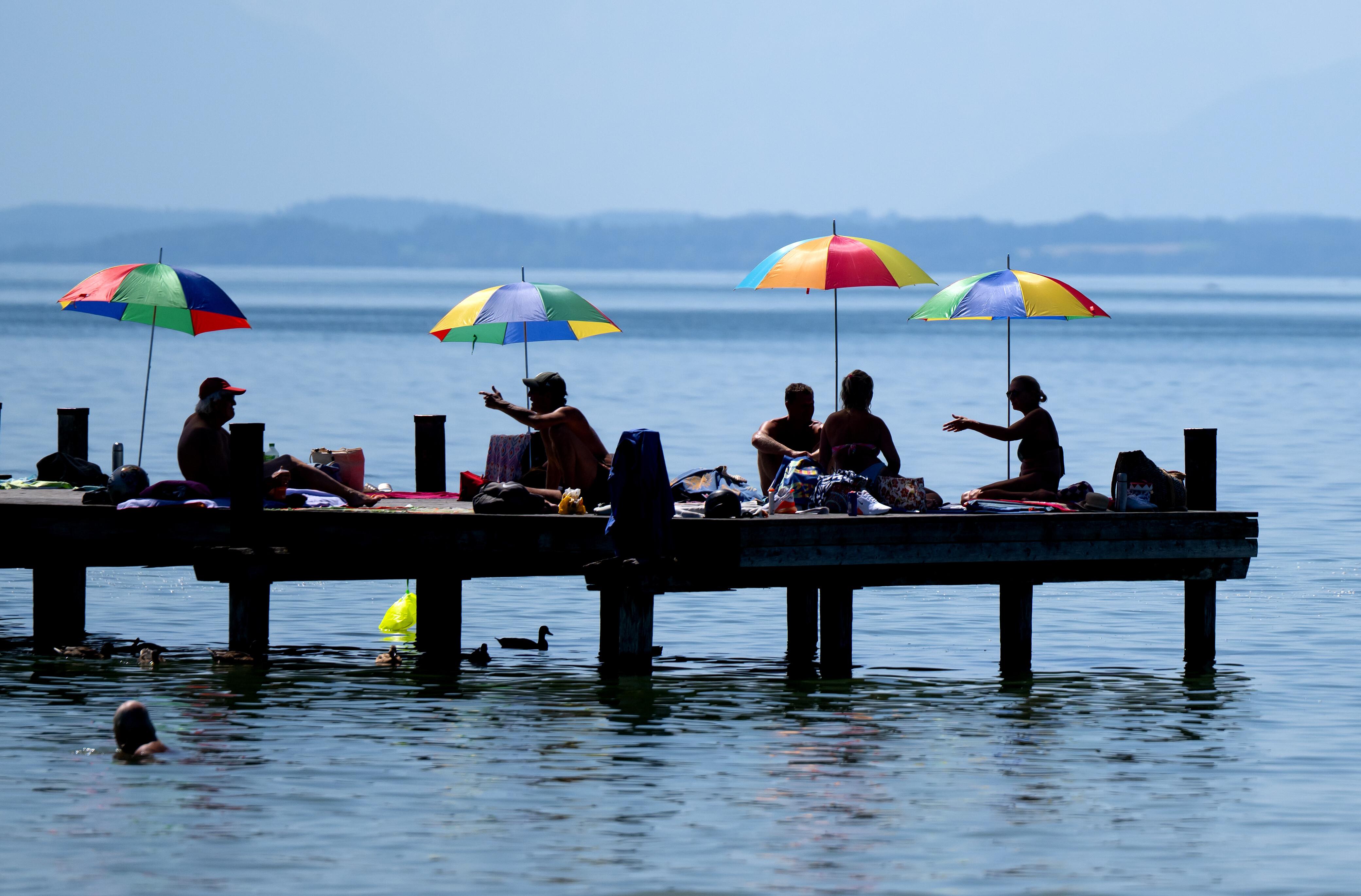 Menschen unter Sonnenschirmen auf einem Steg am Starnberger See