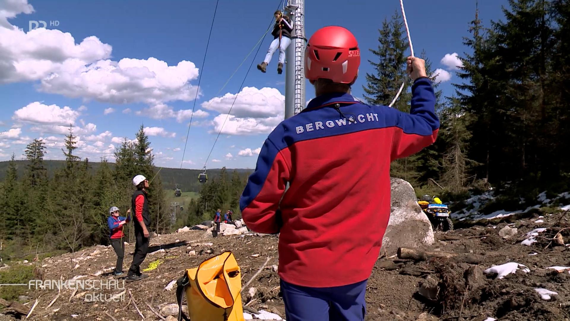 Menschen von der Bergwacht seilen gerade bei einer Übung einen Menschen aus einer Gondel ab.
