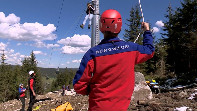 Menschen von der Bergwacht seilen gerade bei einer Übung einen Menschen aus einer Gondel ab. | Bild: BR Menschen von der Bergwacht seilen gerade bei einer Übung einen Menschen aus einer Gondel ab.