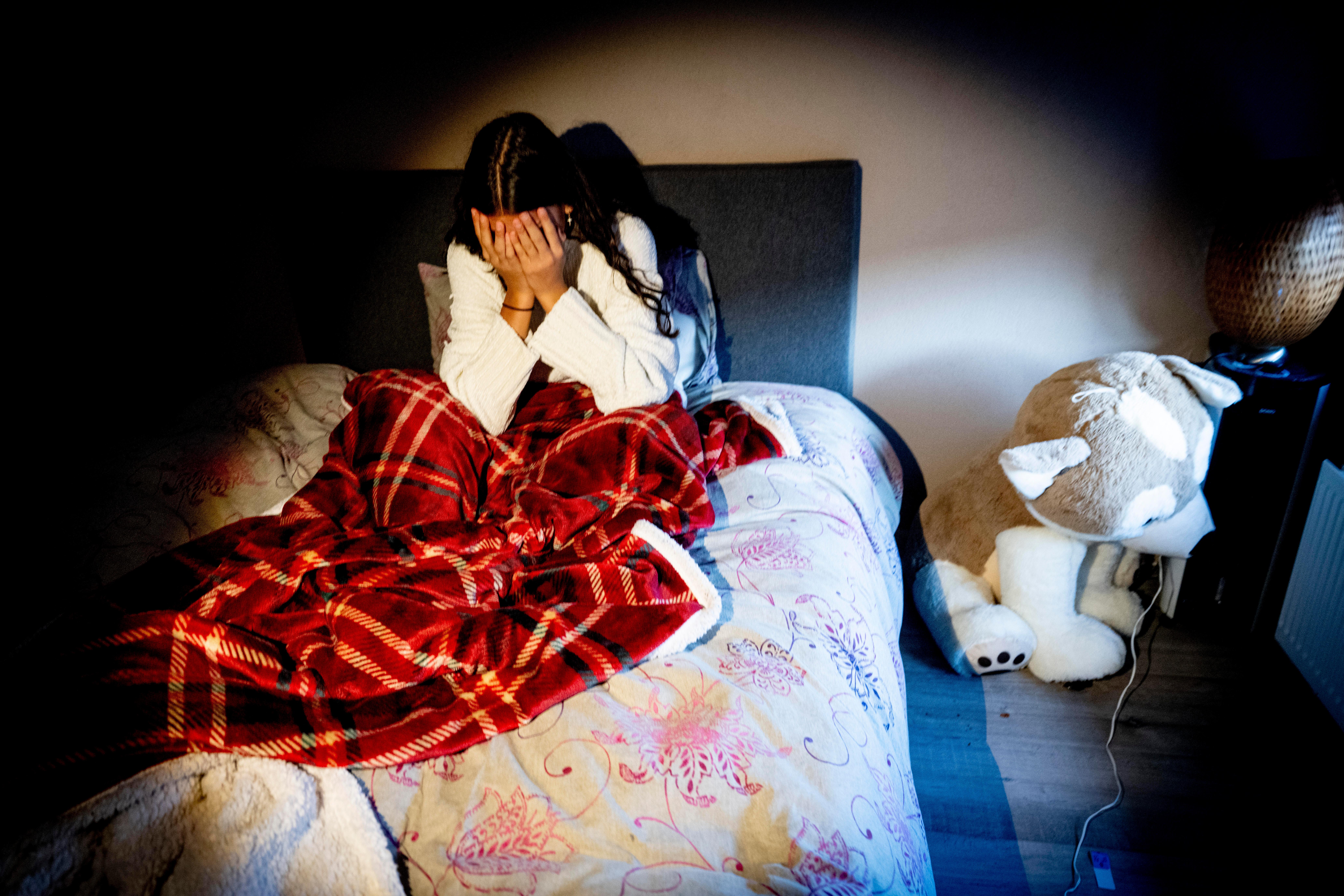 Mädchen im Bett mit Händen vor dem Gesicht.