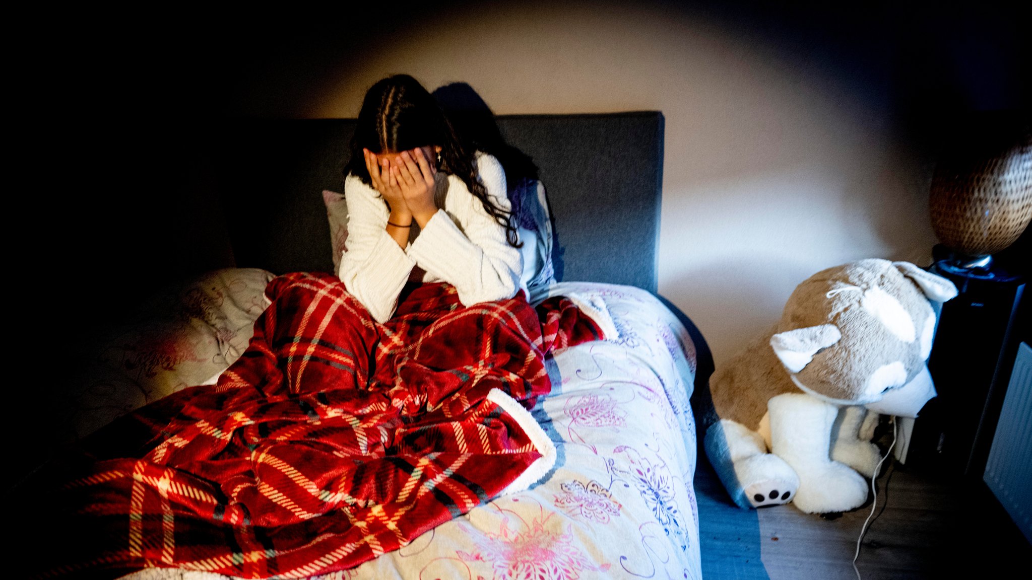 Mädchen im Bett mit Händen vor dem Gesicht.