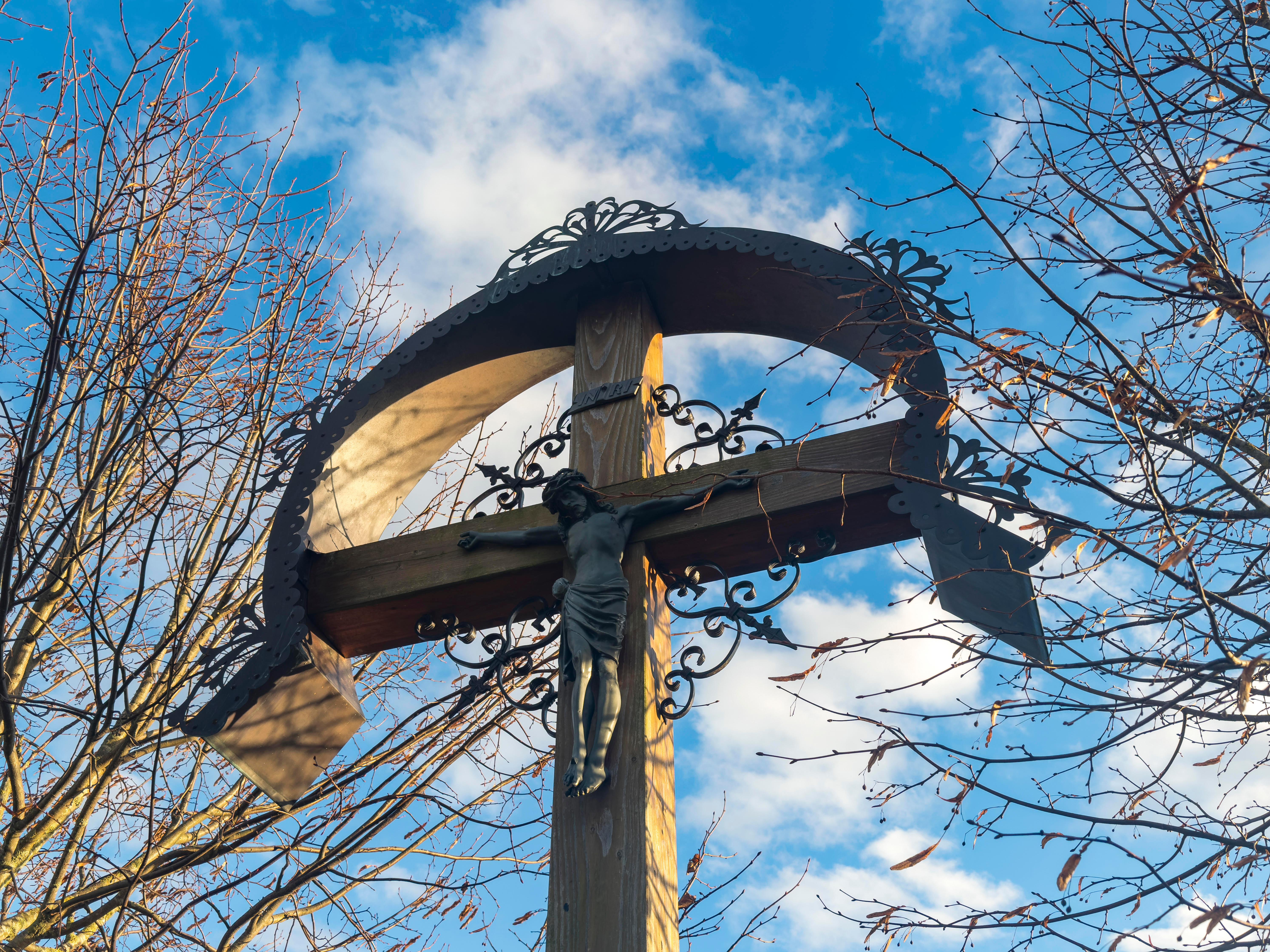 Christliches Kreuz mit einer Jesus Figur an einem Feldweg vor blauem Himmel