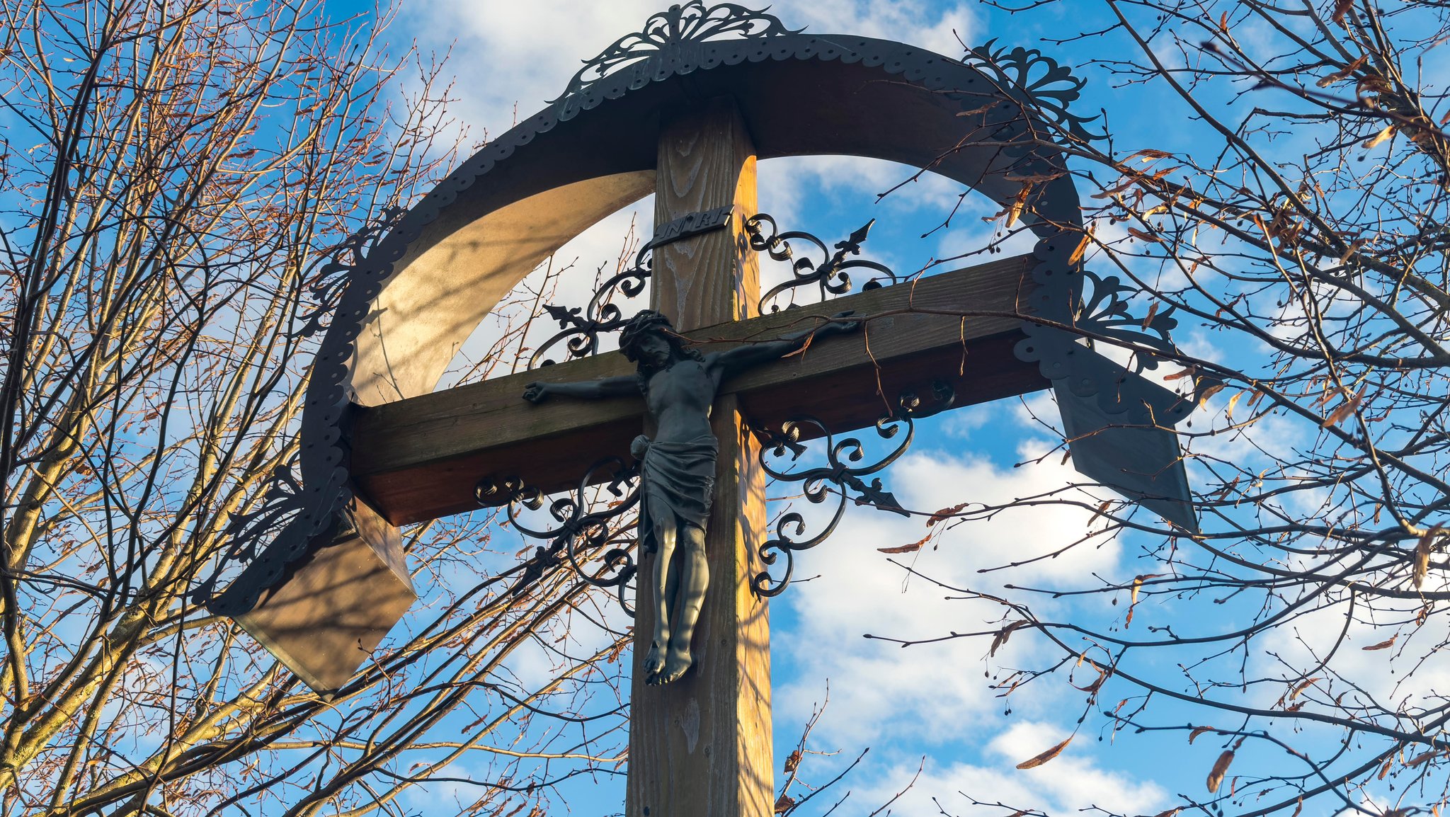 Christliches Kreuz mit einer Jesus Figur an einem Feldweg vor blauem Himmel