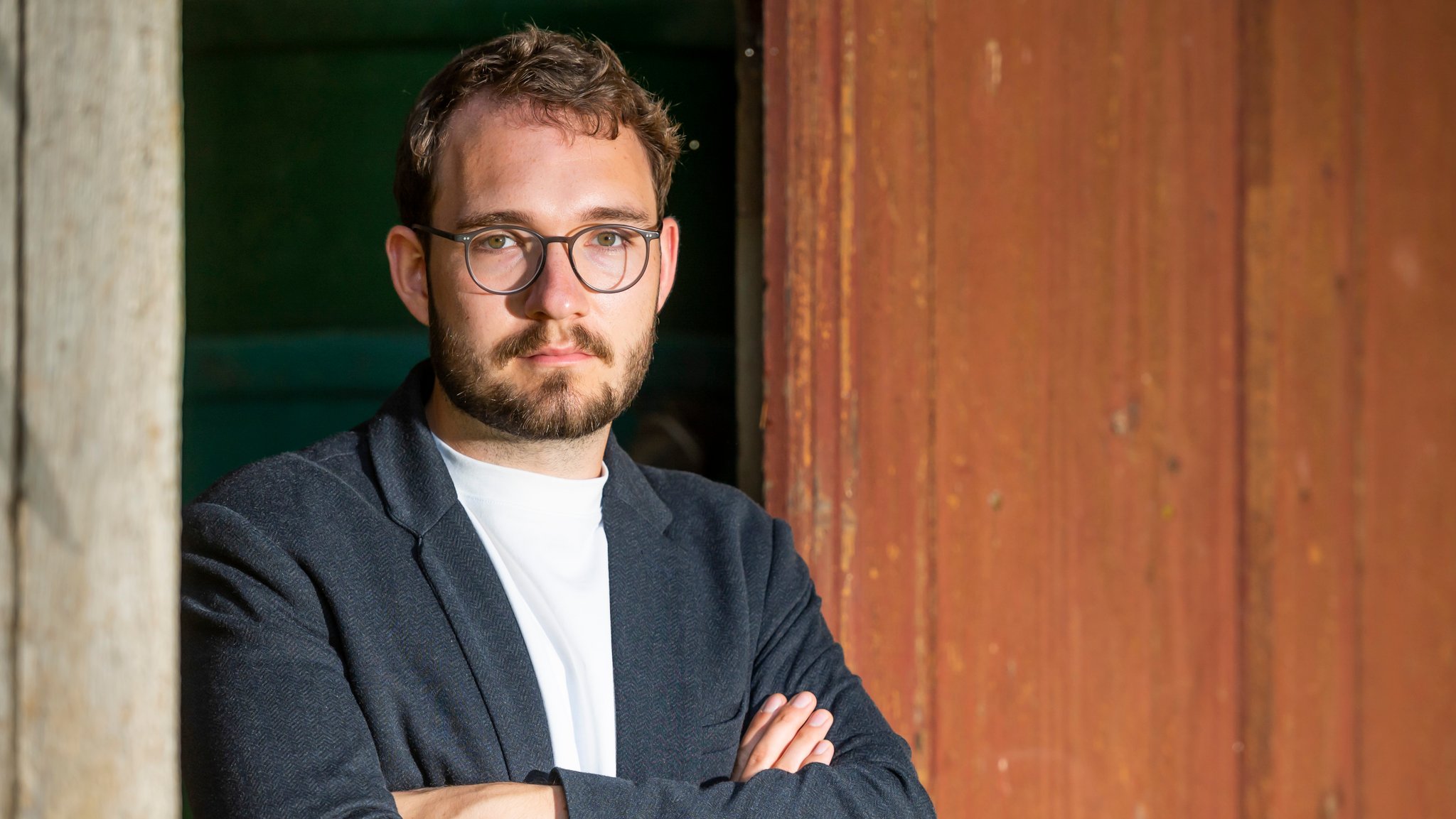 Der Autor und Schriftsteller Lukas Rietzschel lehnt bei einem Fototermin in seinem Wohnort Görlitz mit verschränkten Armen an einer Holztür.