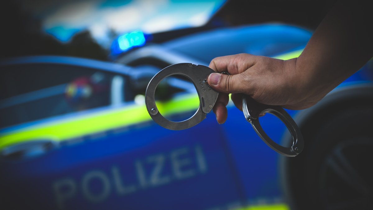 Ein Polizist zeigt Handschellen vor einem Einsatzwagen 