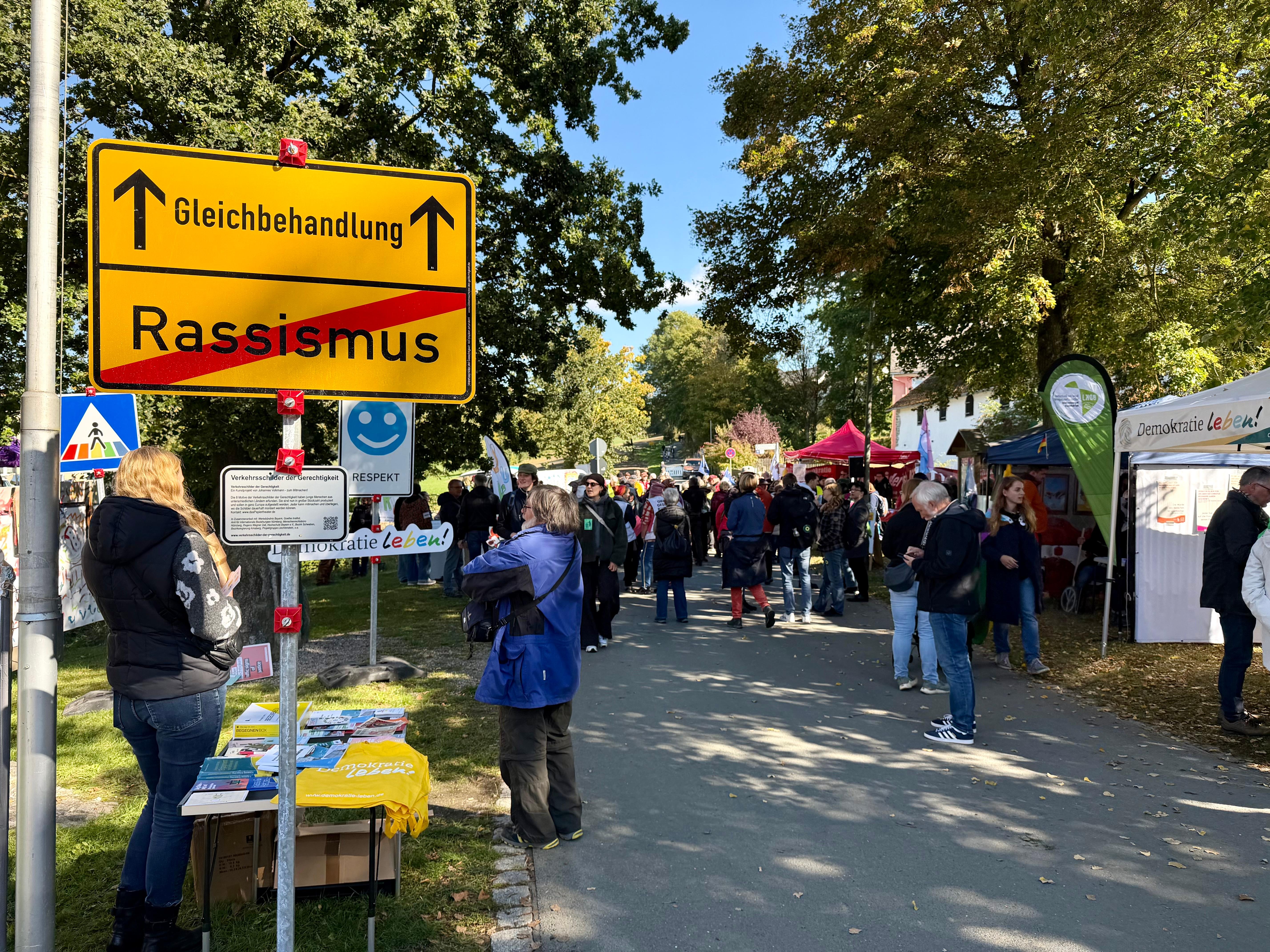 Auf einem selbstgemachten Ortsschild ist das Wort "Rassismus" durchgestrichen und der Weg führt Richtung "Gleichbehandlung".