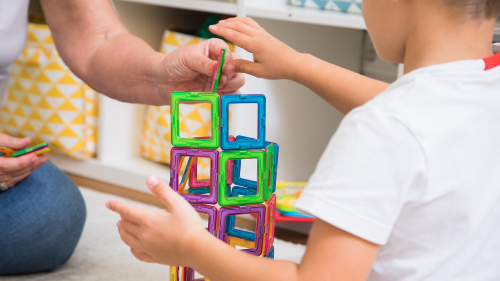 Ein Kind und eine erwachsene Frau sind im Anschnitt zu sehen. Sie bauen einen Turm aus magnetischen Bausteinen.