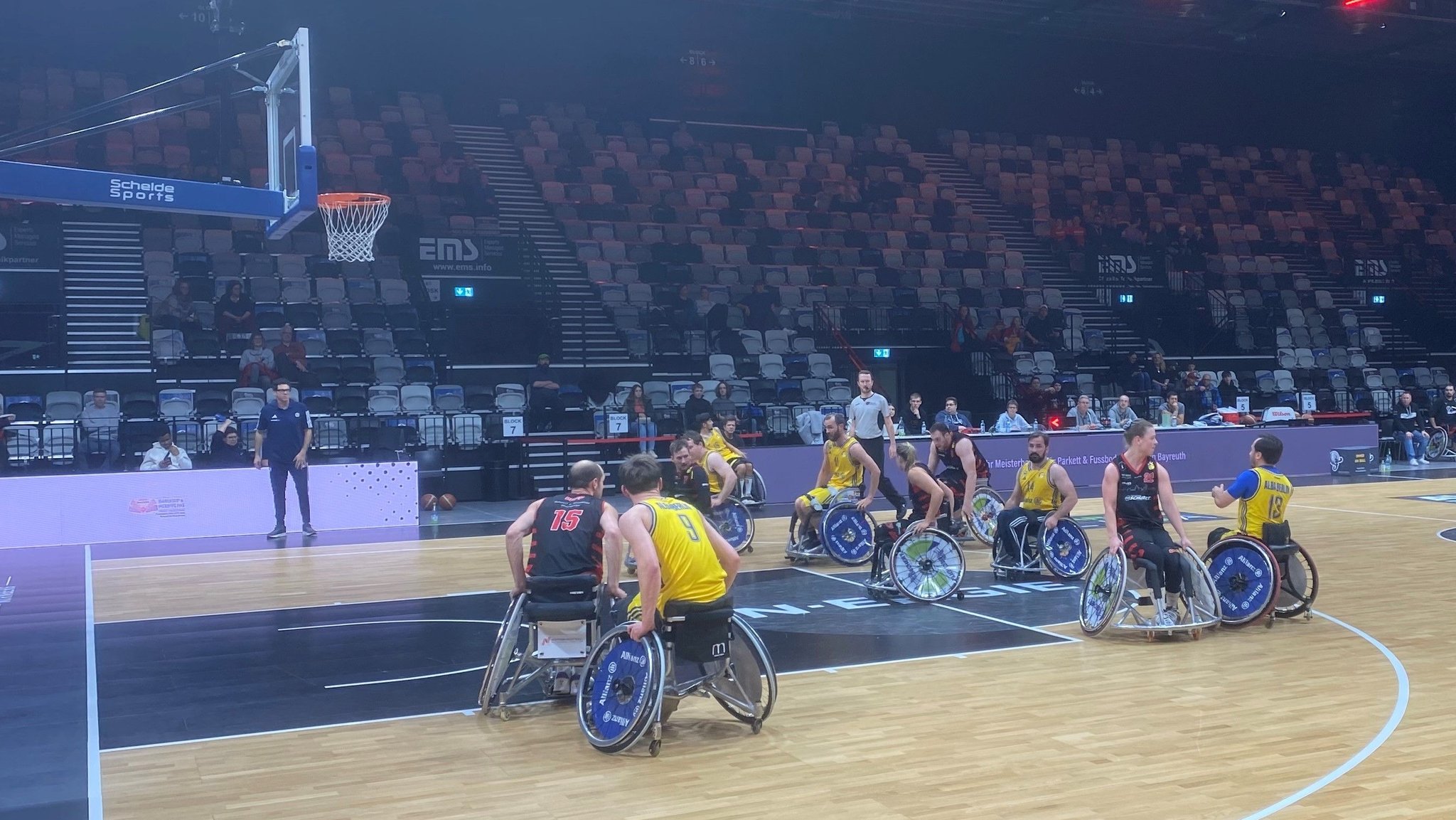 Rollstuhlbasketballer auf dem Spielfeld in einer Halle.