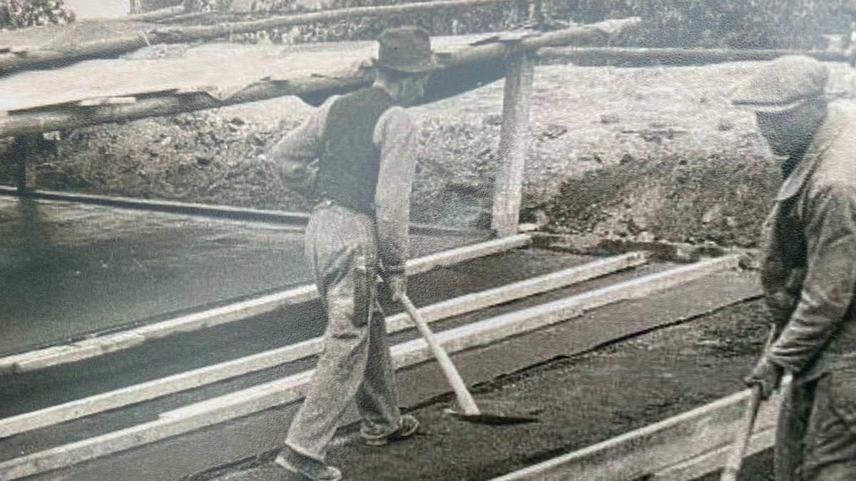 Schwarzweiß-Bild von Bauarbeitern beim Betonieren mit Schaufeln in der Hand.