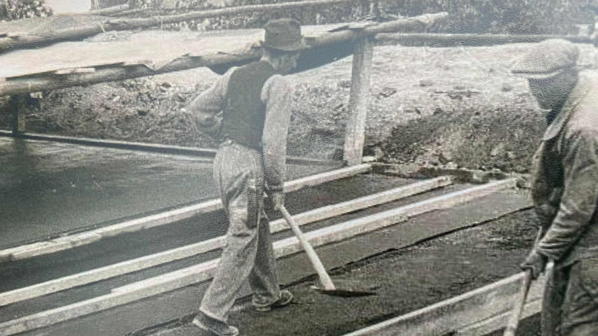 Schwarzweiß-Bild von Bauarbeitern beim Betonieren mit Schaufeln in der Hand.