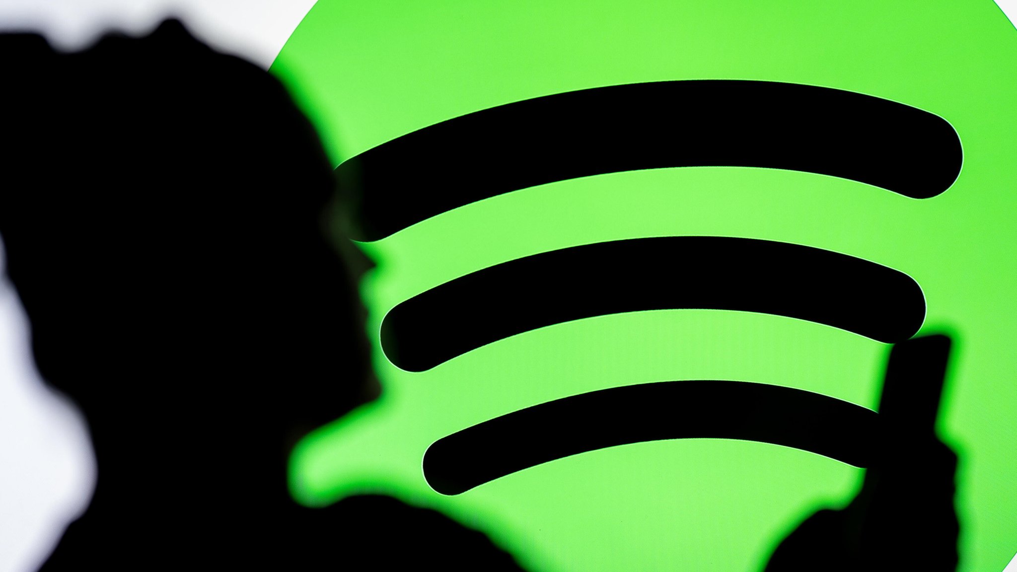 Die Silhouette eines Frauenkopfs zeichnet sich vor einem Spotify-Logo ab. Sie schaut auf ein Mobiltelefon. 