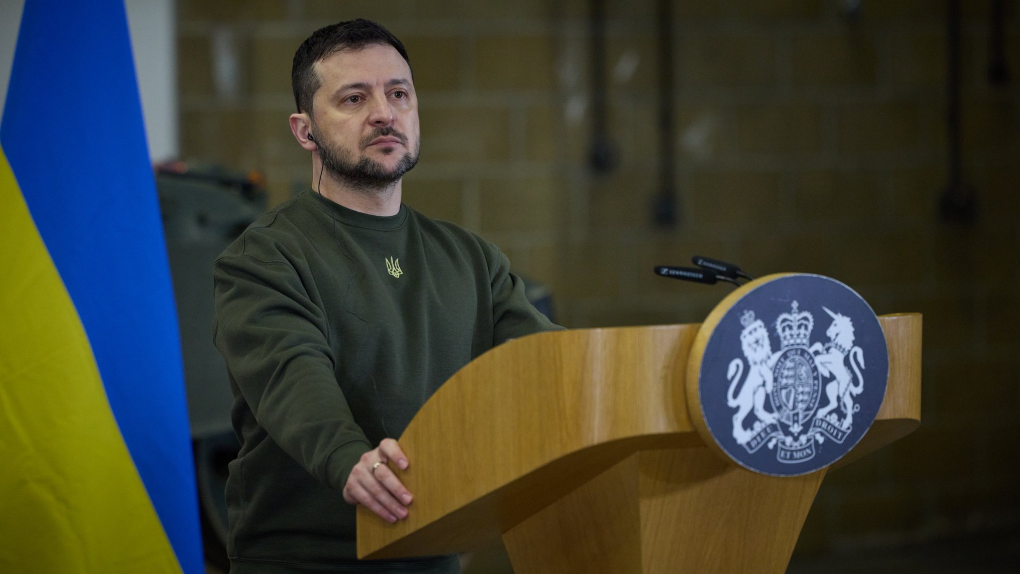 Wolodymyr Selenskyj steht an einem Rednerpult, im Hintergrund hängt eine Ukraine-Flagge.