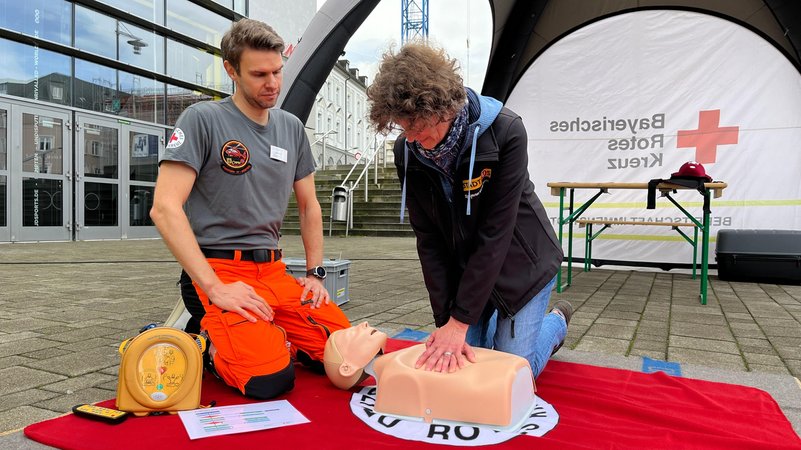 Tanja Kunz kniet vor einer Puppe und übt die Herzdruckmassage – unter Anleitung des neben ihr sitzenden Notarztes. | Bild: BR/Rupert Waldmüller Tanja Kunz kniet vor einer Puppe und übt die Herzdruckmassage – unter Anleitung des neben ihr sitzenden Notarztes.