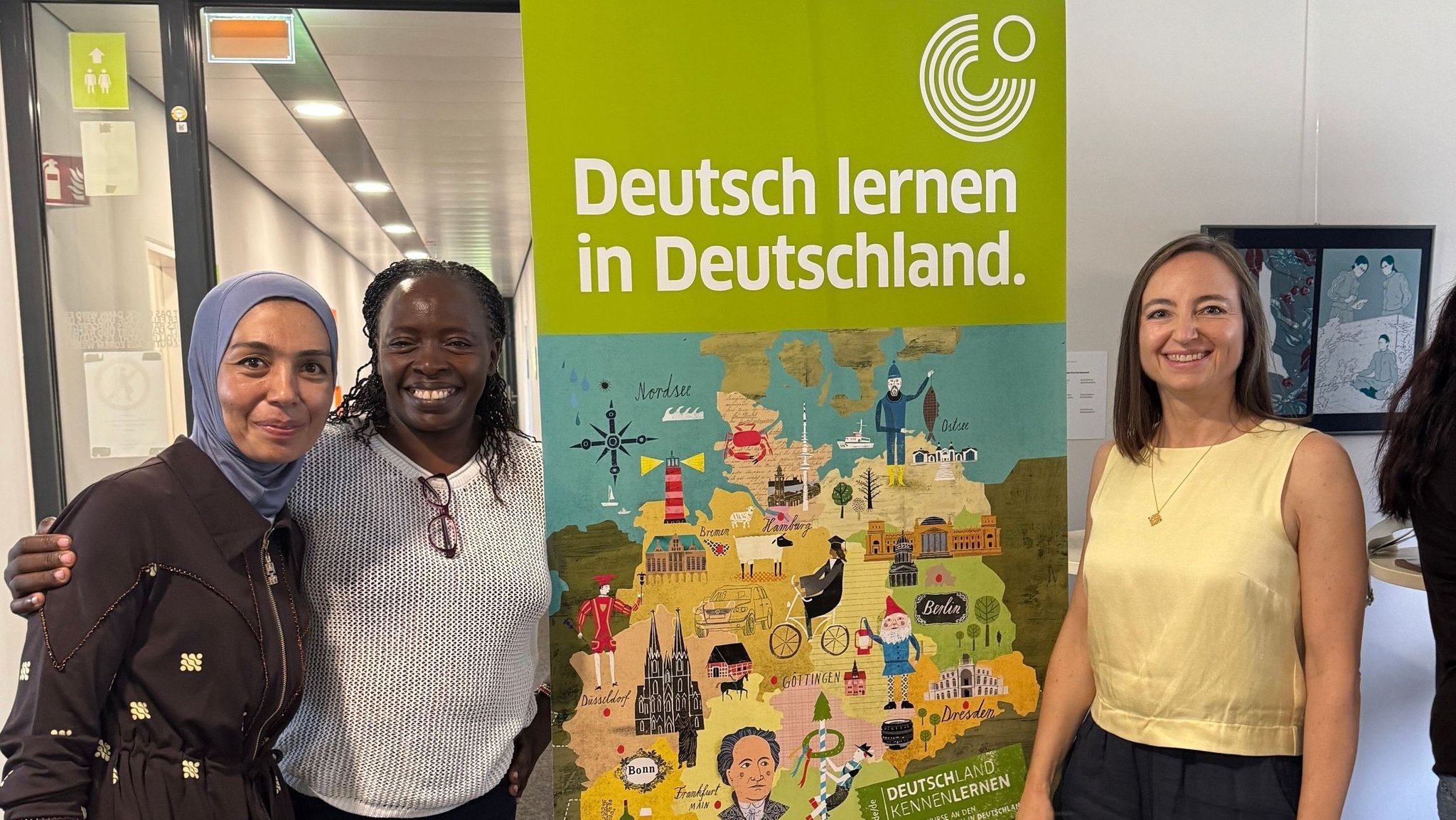 Sprachschüler und die stellvertretende Leiterin des Münchner Goethe-Instituts, Halt, vor einer bunten Deutschlandkarte | Bild: Bayerischer Rundfunk 2026 Sprachschüler und die stellvertretende Leiterin des Münchner Goethe-Instituts, Halt, vor einer bunten Deutschlandkarte