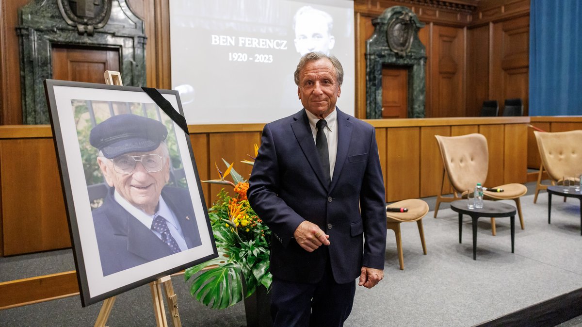 Don Ferencz steht im Saal 600 im Memorium Nürnberger Prozesse neben einem Porträt seines verstorbenen Vaters Benjamin Ferencz. 