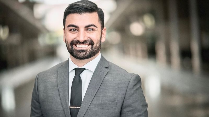 Muhanad Al-Halak steht in einem grauen Anzug in einem Gebäude und lächelt. 
