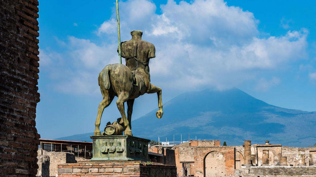 Zentauer-Staue in den Ruinen der durch den Ausbruch des Vesuvs zerstörten antiken Stadt Pompeij, im Hintergrund der Vulkan. Bronzefigur, halb Mensch halb Pferd.