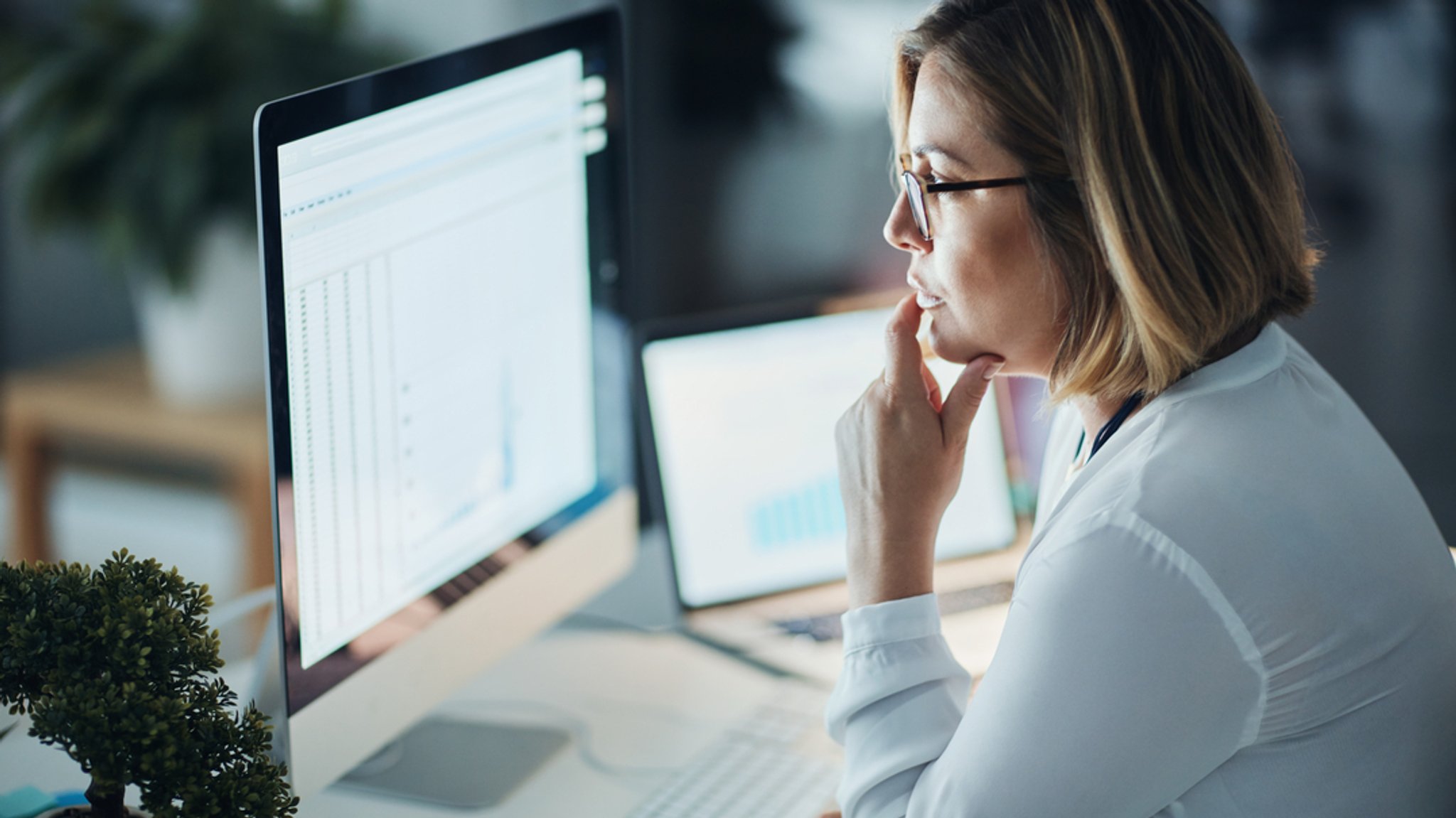 Eine Frau sitzt im Büro vor ihrem Computer und blickt auf einen Bildschirm.