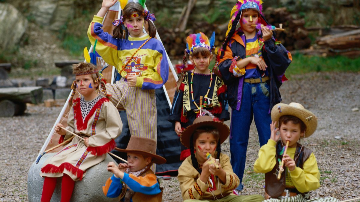 Kinder mit Kopfschmuck und Federn und Cowboyhut spielen Indianer und Cowboy