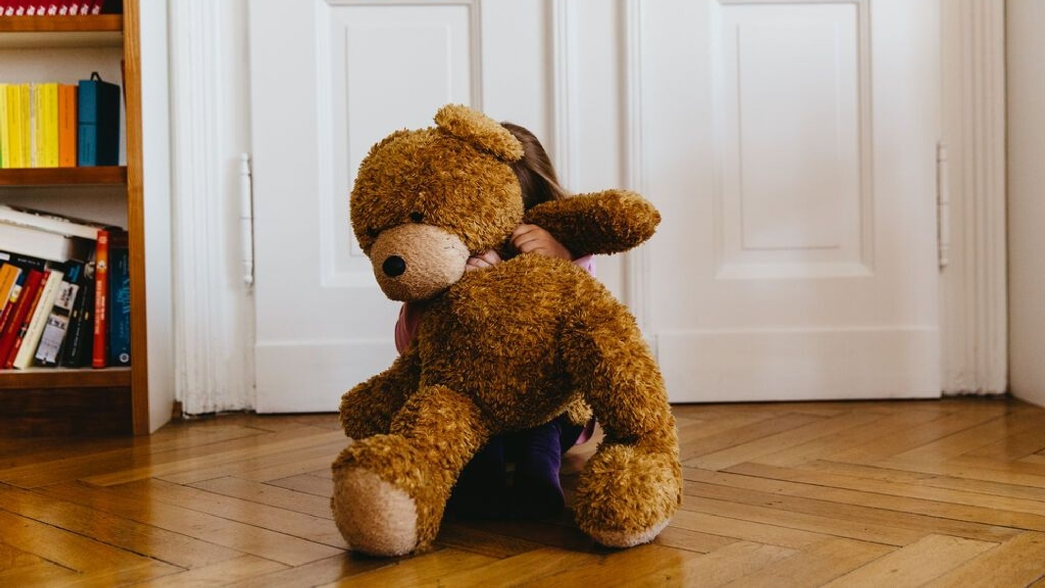 Ein Kind versteckt sich hinter seinem Teddy.