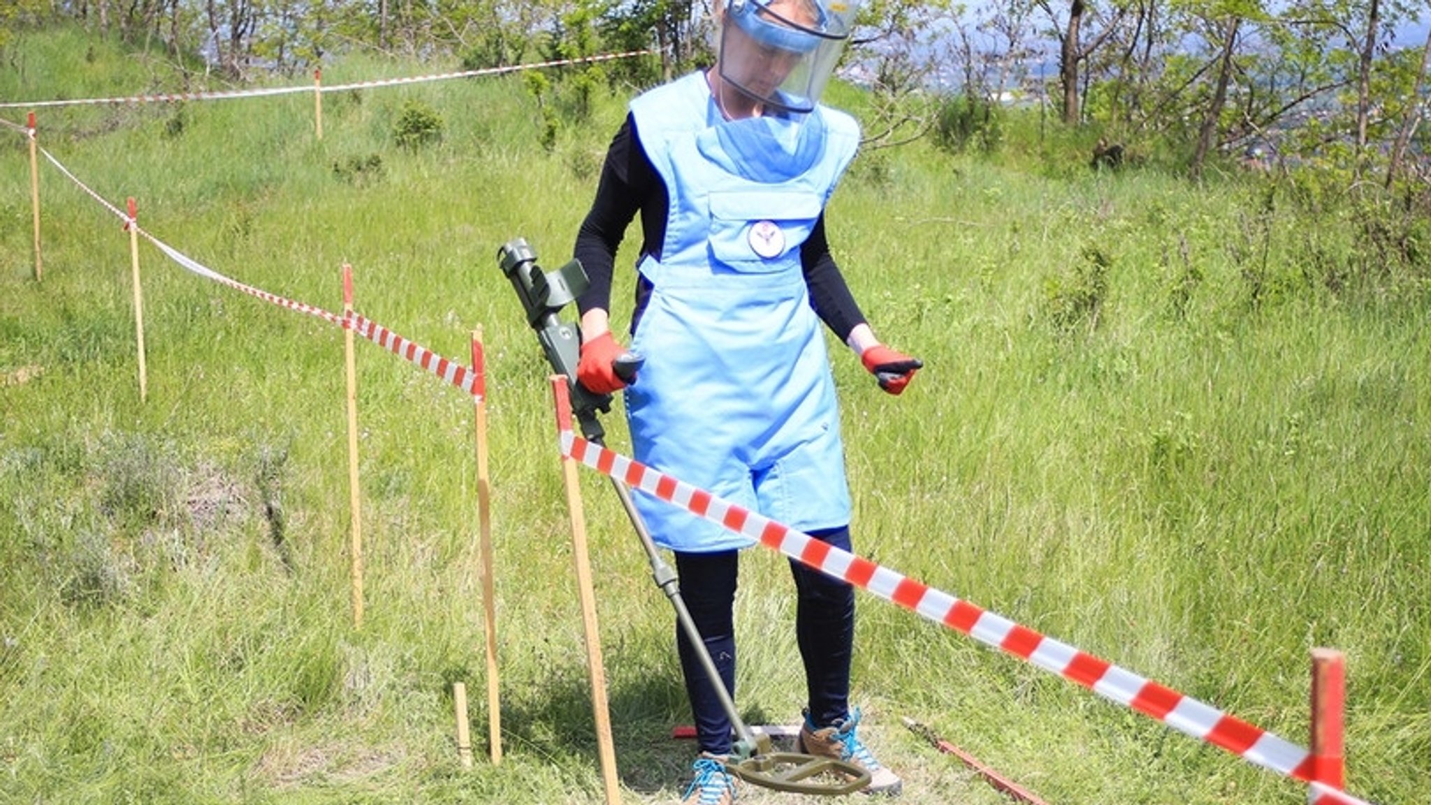 Eine Frau steht mit einem Metalldetektor auf einem markierten Feld bei der Ausbildung zu Minensucherinnen in Peja (Kosovo).