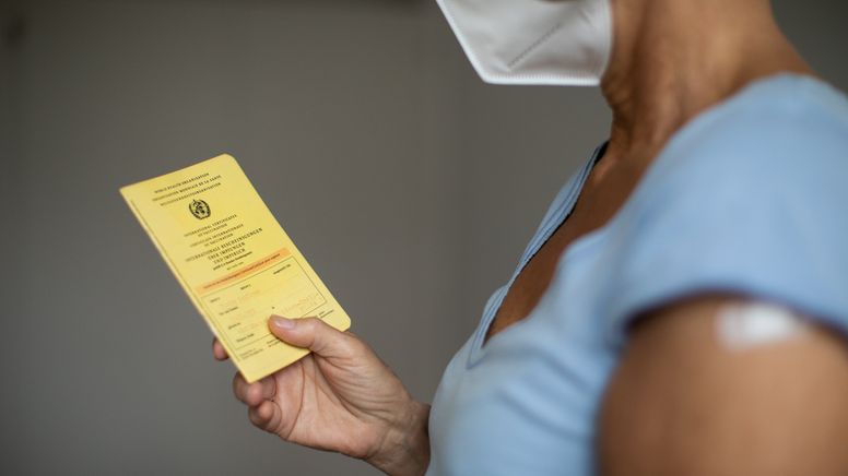 Frau mit Maske hält Impfpass in der Hand | Bild:BR/Johanna Schlüter