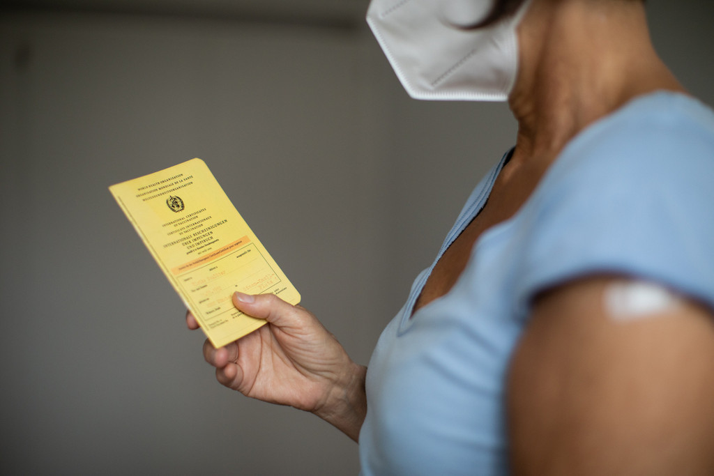 Frau mit Maske hält Impfpass in der Hand