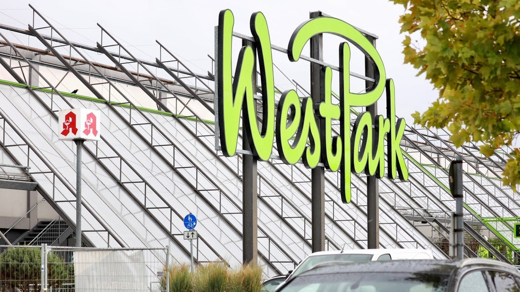 Die Glasfassade des Ingolstäder Einkaufszentrums "Westpark", davor auf Metallpfosten montiert der übermannsgroße Logo-Schriftzug "Westpark" des Einkaufszentrums.